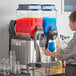 A woman pouring a drink into a Bunn slushy machine.