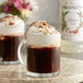 A glass mug of Monin almond flavoring syrup in coffee with whipped cream.