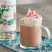 A glass mug of hot chocolate with Monin peppermint syrup and whipped cream.