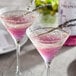 Two martini glasses of pink liquid with lavender flowers on a table in a cocktail bar.