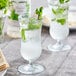 A glass of liquid with ice and Monin Premium Frosted Mint syrup with mint leaves.