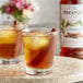 Two glasses of brown liquid with ice and cinnamon sticks and apple slices with Monin Premium Cinnamon Flavoring Syrup.