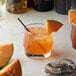 A glass of orange drink with Monin Premium Rock Melon Cantaloupe syrup and fruit slices.