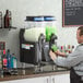 A man pouring green liquid into a Bunn slushy machine.