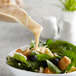 A bowl of salad with blueberries and croutons being poured AAK Select Recipe Honey Mustard Dressing.