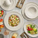 An Acopa Warm Gray scalloped porcelain platter on a table with food and plates.