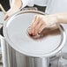 A person's hand holding a silver lid over a large silver pot.