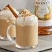 A glass mug of Monin spiced brown sugar flavoring syrup with whipped cream and a cinnamon stick.