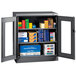 A dark gray Tennsco metal storage cabinet with C-Thru doors holding boxes and papers.
