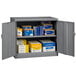 A metal Tennsco dark gray storage cabinet with solid doors holding many boxes.