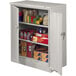 A light gray Tennsco deluxe storage cabinet with solid doors filled with items.