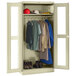 A putty Tennsco unassembled industrial wardrobe cabinet with clothes and shoes on shelves and a coat rack inside with C-Thru doors.