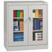 A light gray Tennsco storage cabinet with C-Thru doors holding boxes and paper.
