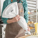 A person in an apron holding a Choice plastic coated canvas pastry bag.