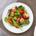 A Arcoroc white porcelain side plate with a salad on a table.