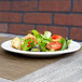 An Arcoroc white porcelain side plate with salad on a table.