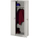 A light gray metal Tennsco wardrobe cabinet with solid doors holding a red shirt and a helmet.