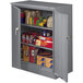 A dark gray Tennsco deluxe storage cabinet with solid doors filled with boxes and other items.