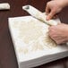 A person folding a gold Hoffmaster linen-like dinner napkin.
