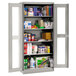 A light gray Tennsco metal storage cabinet with C-Thru doors and shelves full of a variety of products.