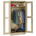 A beige Tennsco wardrobe cabinet with clothes and hats behind C-Thru doors.