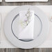 A silver Carlisle charger plate with a napkin and flowers on it.