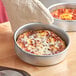 A person wearing a glove holding a deep dish pizza in a Choice aluminum pan.