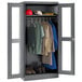 A dark gray metal Tennsco wardrobe cabinet with C-Thru doors holding clothes and shoes.