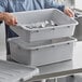 A man holding a gray Choice polypropylene bus tub full of silverware.