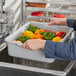 A person holding a gray Choice polypropylene bus tub of vegetables.