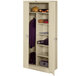 A white metal Tennsco combination cabinet with solid doors and shelves holding a coat and jacket.