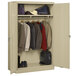 A sand Tennsco metal wardrobe cabinet filled with clothes and shoes.