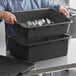 A man holding a black Choice polypropylene bus tub full of silverware.