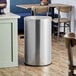 A Lancaster Table & Seating stainless steel trash can with decorative accents.