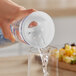 A hand using a Front of the House Drinkwise Fast / Slow Pour Carafe Lid to pour water into a glass.