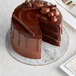 An Enjay round cardboard marble and wood reversible cake board with a chocolate cake on it in a bakery display with a slice missing.