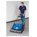 A man in a blue shirt using a Powr-Flite wide area vacuum to clean a carpet.