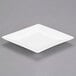 A white porcelain coupe dinner plate with a square cut out on a gray surface.