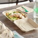 World Centric compostable clamshell containers holding salad and chicken on a table.