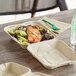 A World Centric compostable fiber clamshell container with a salad on a table.