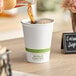 A person pouring coffee into a World Centric white compostable paper hot cup.