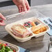 A clear compostable three-compartment PLA lid being placed on a divided food container.