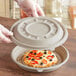 A person's hands in gloves holding a World Centric compostable fiber pizza lid over a pizza