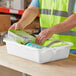 A man in a safety vest putting a box in a white Lavex utility bin.