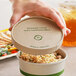 A hand holding a World Centric compostable paper container with a Kraft lid.