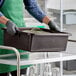 A large brown polyethylene utility bin being carried by a person wearing gloves and an apron.