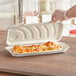 A hand holding a World Centric compostable fiber flat bread container with pizza inside.