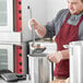 A man in a red apron using a Choice stainless steel ladle to pour soup into a pot.