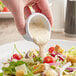 A person pouring Kraft Creamy Caesar Dressing on a salad.