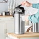 A person pouring coffee into a stainless steel Bunn airpot.